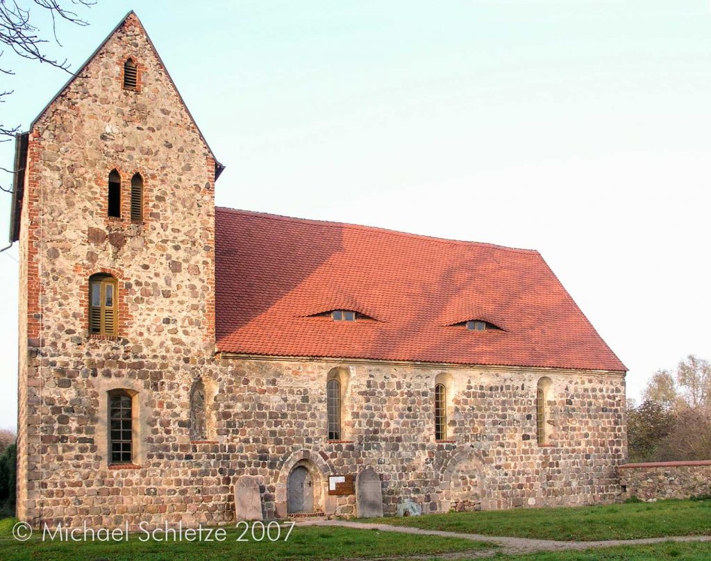 Schmale hoch ansetzende Fenster und ein zweistufiges Feldsteinportal: Die Südseite der Neuendorfer Kirche